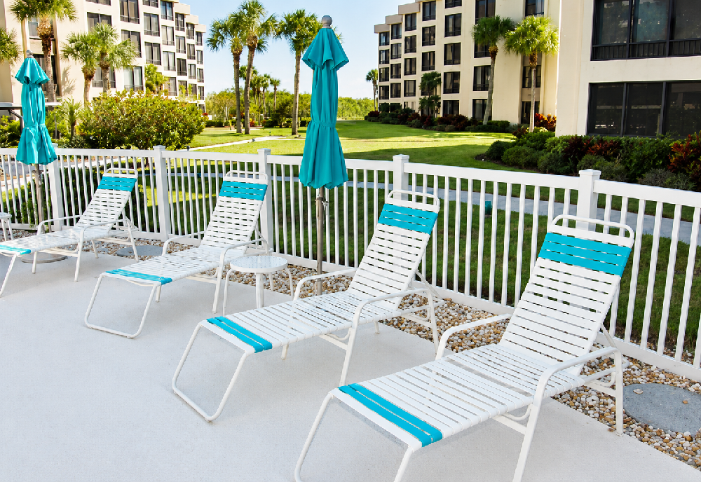White commercial strap chaise lounges with turquoise accents arranged beside a resort swimming pool for stylish guest relaxation.